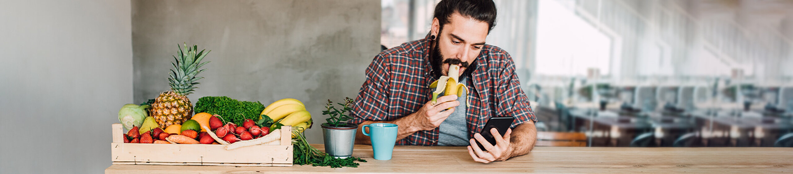 Mann sitzt neben Obstkorb und isst einen Banane